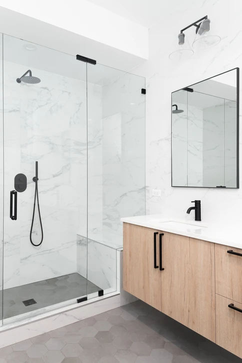 Belle salle de bains moderne et luxueuse avec armoire en bois clair, douche de plain-pied avec carrelage en marbre, robinets et quincaillerie noirs