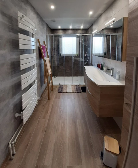 Salle de bain moderne avec douche à l'italienne vitrée, meuble vasque suspendu en bois, miroir éclairé et sèche-serviettes design blanc