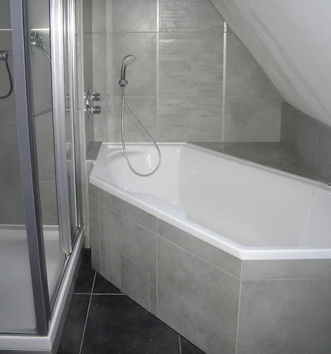 Salle de bain moderne sous combles avec baignoire d'angle blanche et cabine de douche vitrée