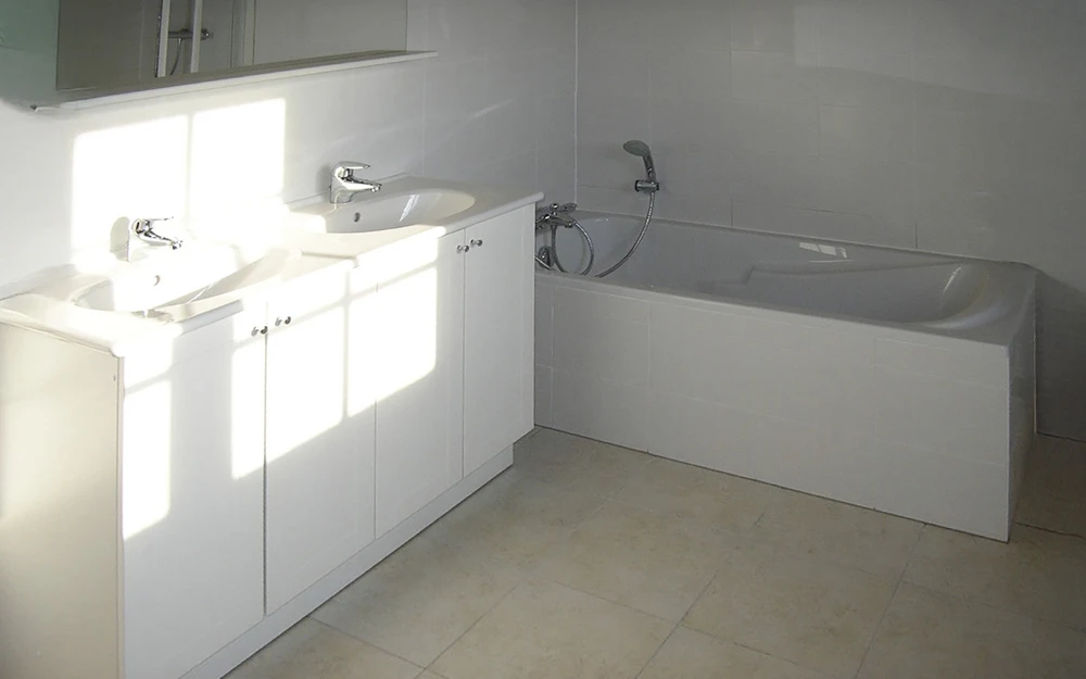 Salle de bain moderne sous combles avec baignoire d'angle blanche et cabine de douche vitrée