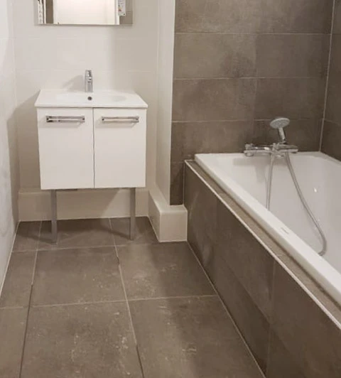 Salle de bain moderne sous combles avec baignoire d'angle blanche et cabine de douche vitrée