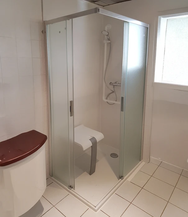 Intérieur de douche moderne avec paroi vitrée transparente et pommeau de douche chromé en fonctionnement, eau ruisselant sur carrelage mural gris clair