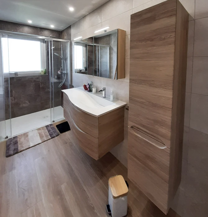Salle de bain moderne avec douche à l'italienne vitrée, meuble vasque suspendu en bois clair à tiroirs, miroir rectangulaire rétroéclairé LED