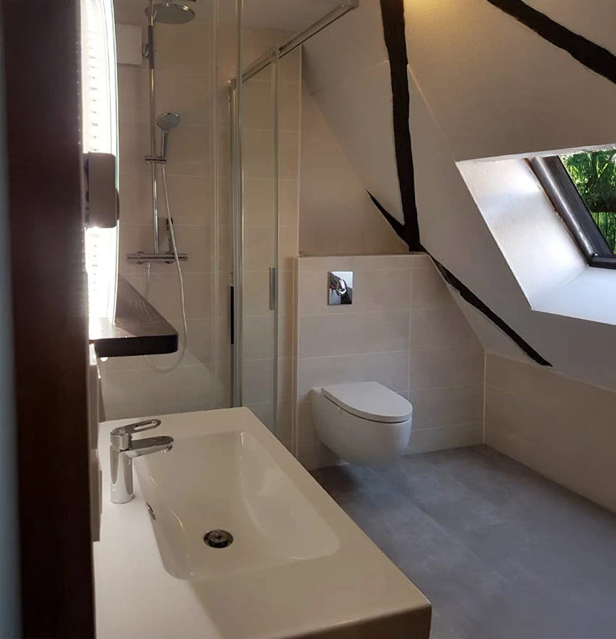 Salle de bain moderne avec douche à l'italienne vitrée, meuble vasque suspendu en bois naturel avec plan blanc intégré, colonne de rangement assortie et miroir éclairé