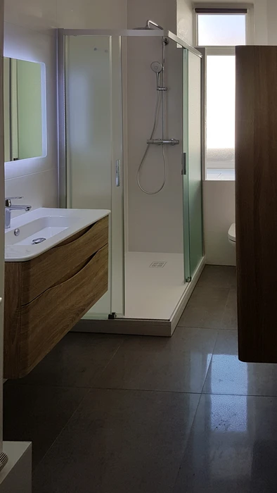 Salle de bain moderne sous combles avec baignoire d'angle blanche et cabine de douche vitrée