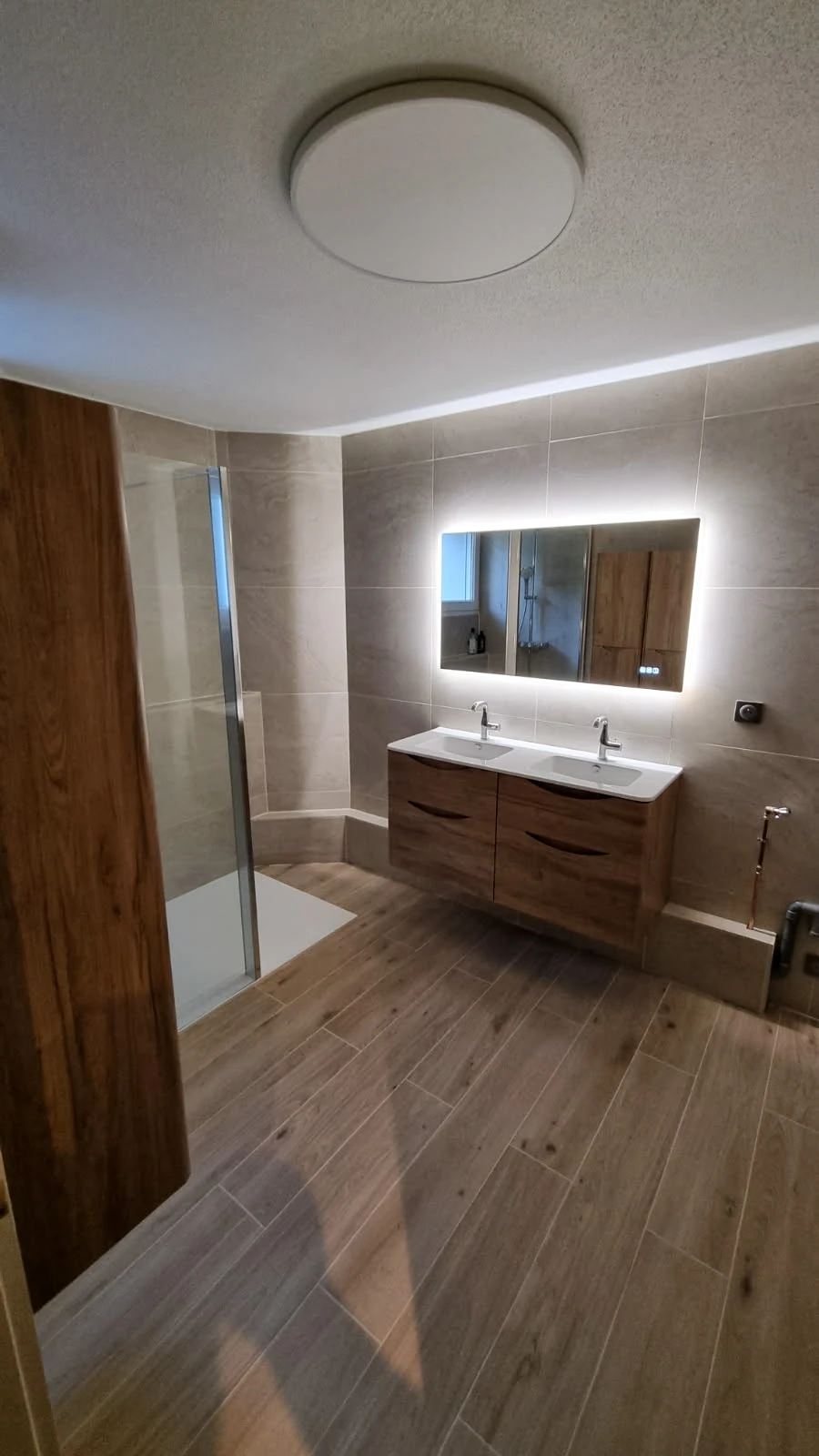 Salle de bain moderne sous combles avec baignoire d'angle blanche et cabine de douche vitrée