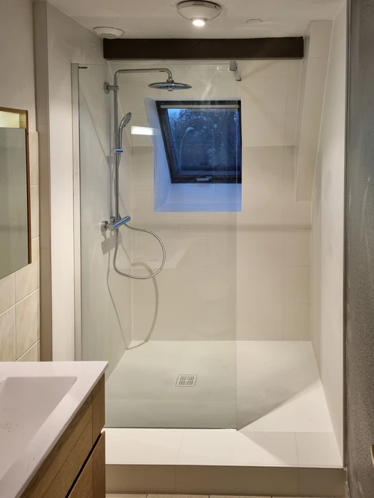 Salle de bain moderne sous combles avec baignoire d'angle blanche et cabine de douche vitrée