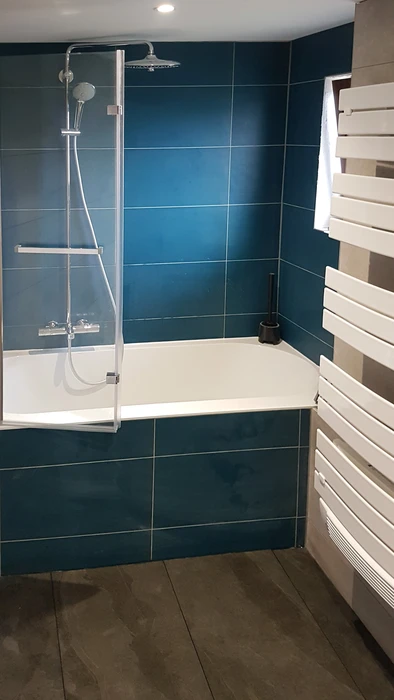 Salle de bain moderne sous combles avec baignoire d'angle blanche et cabine de douche vitrée