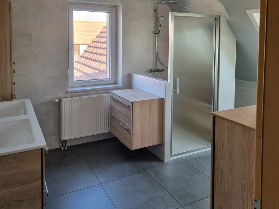 Salle de bain moderne sous combles avec baignoire d'angle blanche et cabine de douche vitrée