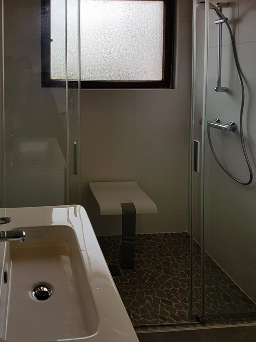 Salle de bain moderne avec baignoire d'angle équipée d'un pare-douche en verre, WC suspendu blanc, meuble vasque suspendu blanc avec plan de toilette intégré et robinetterie chromée