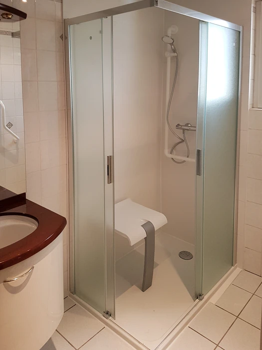 Intérieur de douche moderne avec paroi vitrée transparente et pommeau de douche chromé en fonctionnement, eau ruisselant sur carrelage mural gris clair