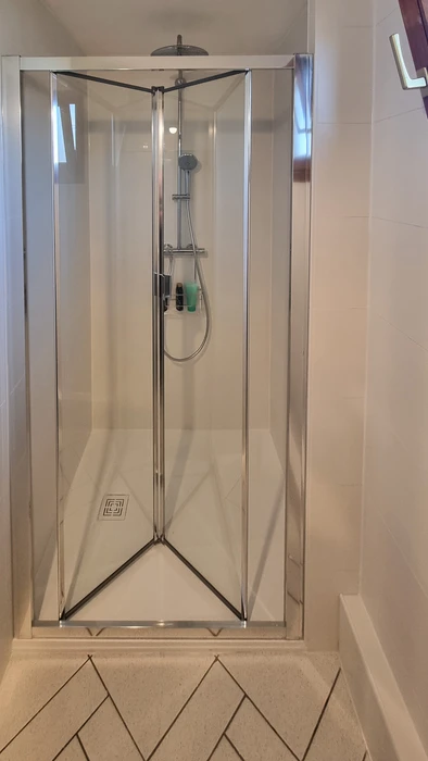 Salle de bain moderne avec douche à l'italienne vitrée, meuble vasque suspendu en bois naturel avec plan blanc intégré, colonne de rangement assortie et miroir éclairé