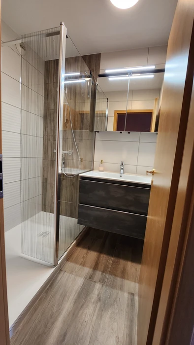 Salle de bain moderne sous combles avec baignoire d'angle blanche et cabine de douche vitrée