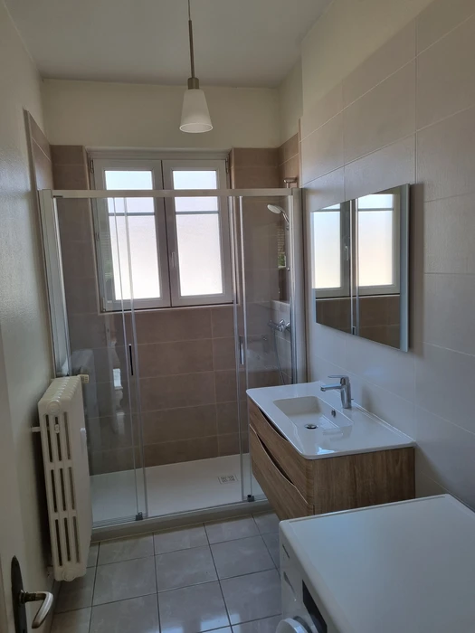 Salle de bain moderne sous combles avec baignoire d'angle blanche et cabine de douche vitrée