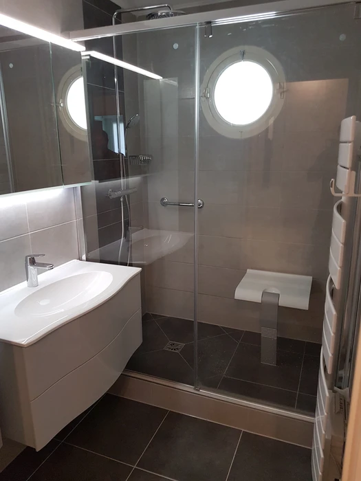 Salle de bain moderne avec baignoire d'angle équipée d'un pare-douche en verre, WC suspendu blanc, meuble vasque suspendu blanc avec plan de toilette intégré et robinetterie chromée