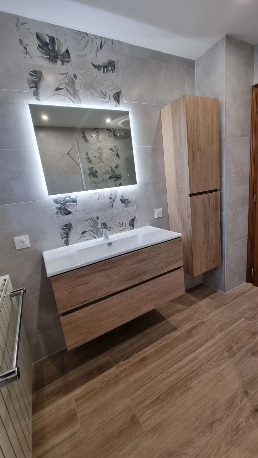Salle de bain moderne avec douche à l'italienne vitrée, meuble vasque suspendu en bois naturel avec plan blanc intégré, colonne de rangement assortie et miroir éclairé